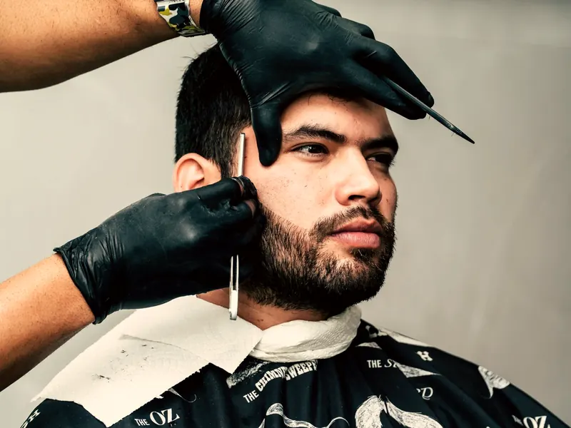 Barbeiro de luvas acertando a barba de um cliente