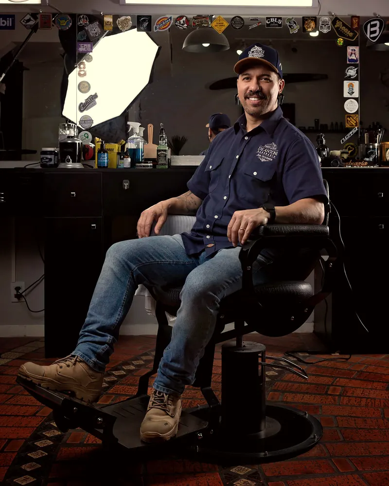 Dono de barbearia sorrindo, sentado na cadeira de barbeiro