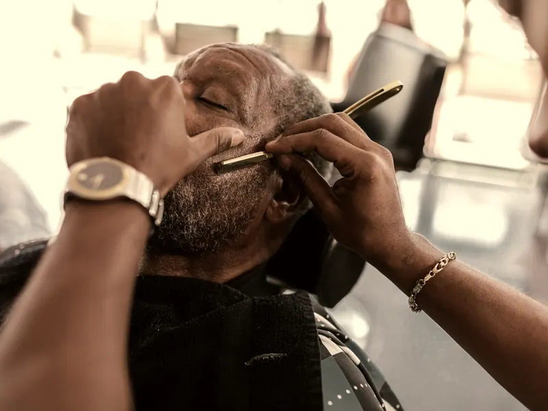 Barbeiro fazendo a barba de um cliente com navalha